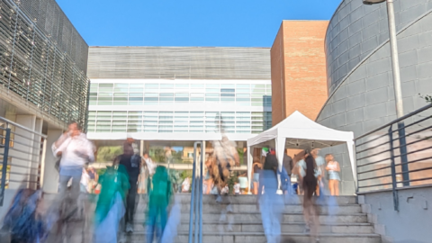 People walking up the steps outside a modern building of Roma Tre University’s Law Department with large windows and brick elements, on a clear sunny day.