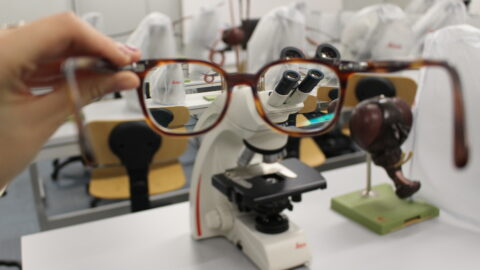 A person holds a pair of glasses in front of him framing the optical laboratory